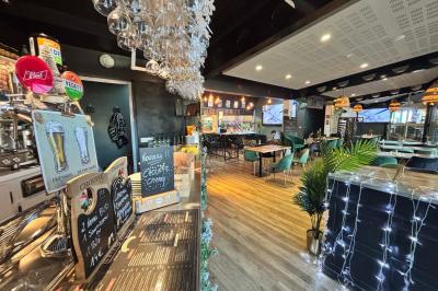 Entrée d'un café avec une grande terrasse, un parasol orange et des meubles en osier sous un ciel bleu.