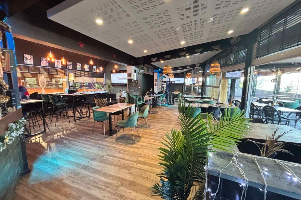 Salle de restaurant moderne avec tables, chaises, plantes décoratives et éclairage chaleureux.