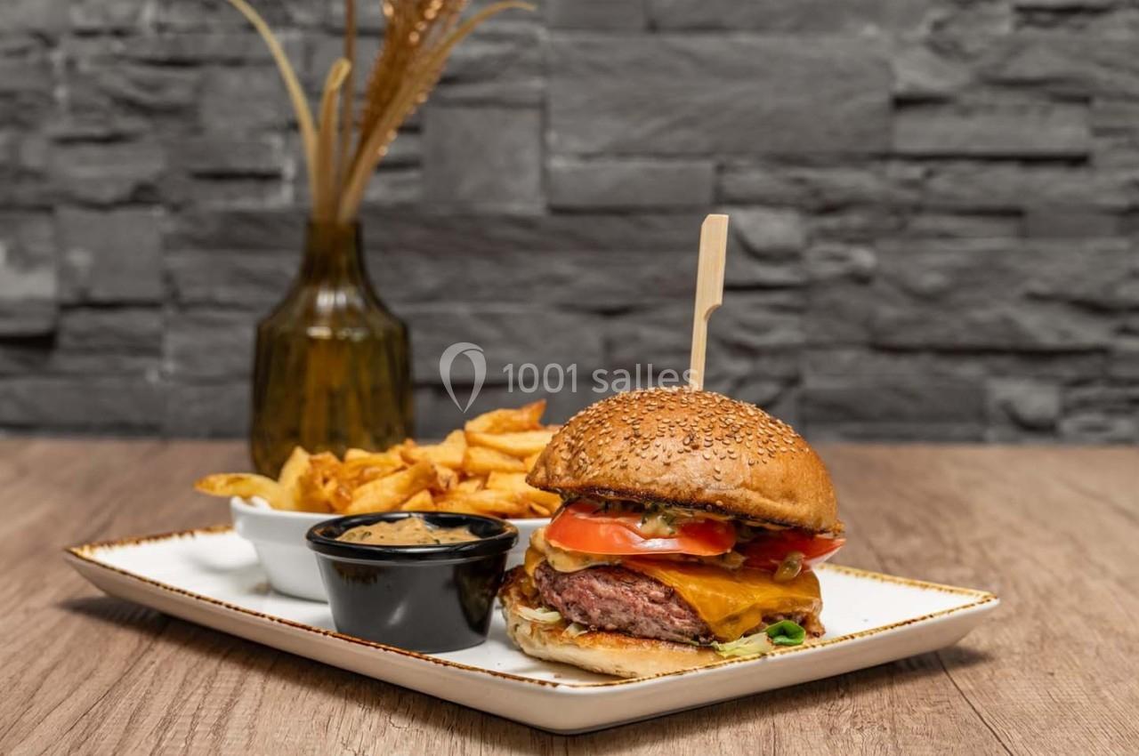 Burger garni de fromage, tomate et salade, accompagné de frites et d'une sauce, servi sur une assiette blanche.
