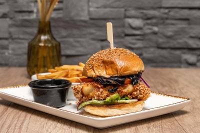 Entrée d'un café avec une grande terrasse, un parasol orange et des meubles en osier sous un ciel bleu.