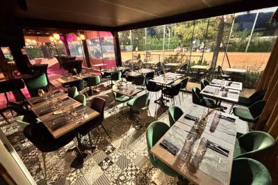 Entrée d'un café avec une terrasse équipée d'un parasol orange et des fauteuils en osier, sous un ciel ensoleillé.