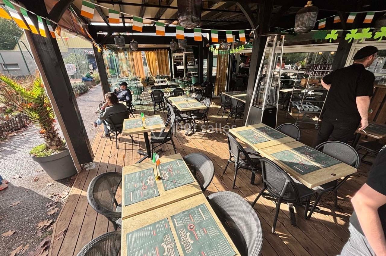 Terrasse d'un restaurant avec tables dressées, décorations aux couleurs irlandaises et clients assis en arrière-plan.