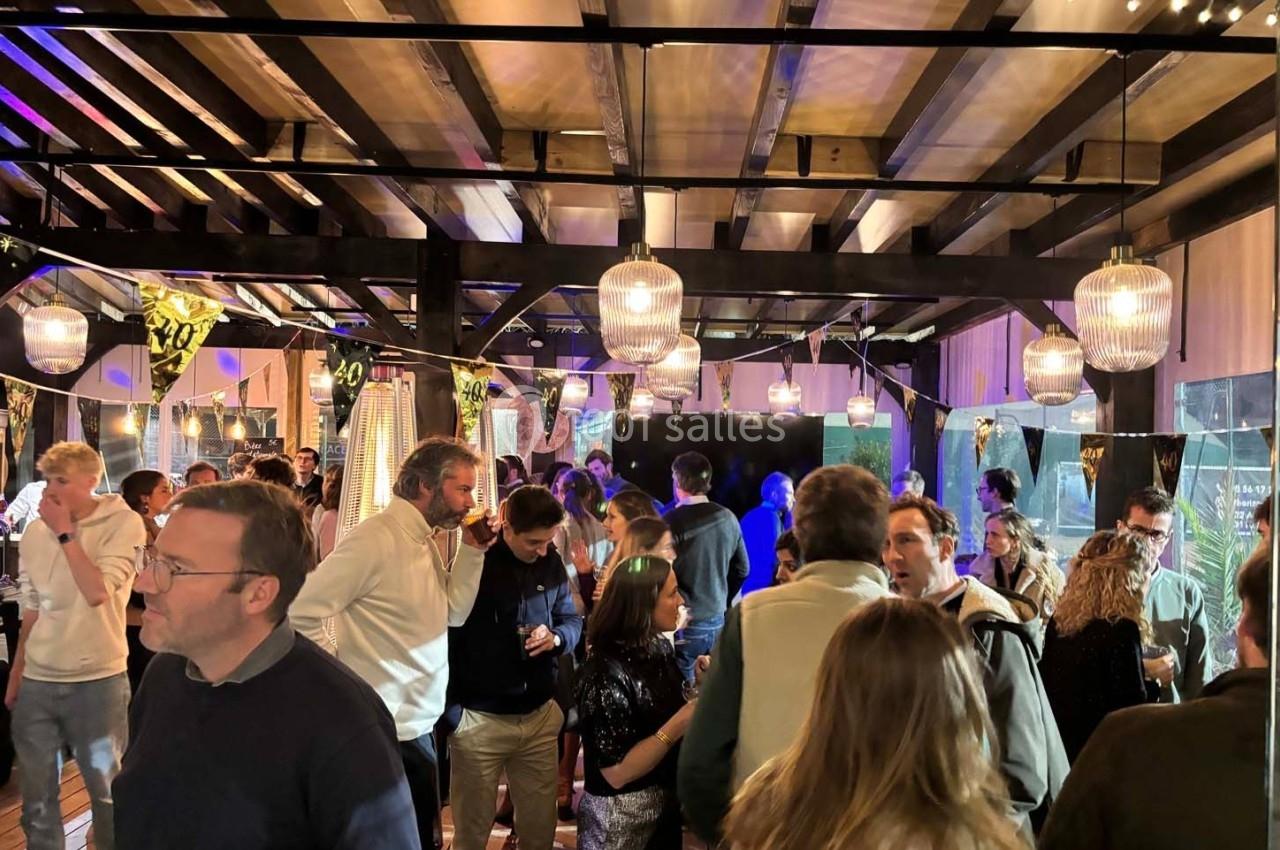 Groupe de personnes discutant dans un espace intérieur éclairé, décoré de guirlandes lumineuses et de ballons.