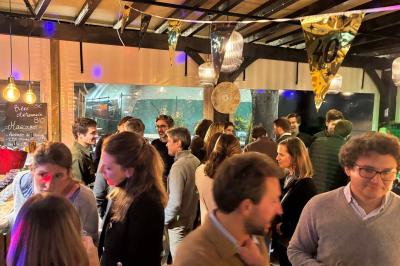 Entrée d'un café avec une terrasse équipée d'un parasol orange et des fauteuils en osier, sous un ciel ensoleillé.