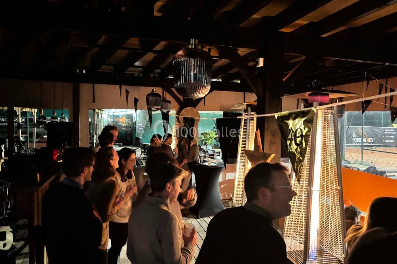 Des personnes rassemblées dans un espace couvert, éclairé par des lampes chauffantes et une lumière tamisée.