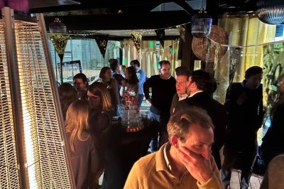 Entrée d'un café avec une terrasse équipée d'un parasol orange et des fauteuils en osier, sous un ciel ensoleillé.