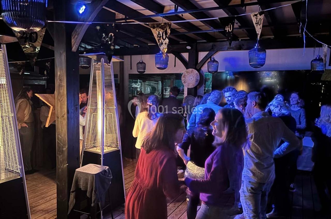 Groupe de personnes discutant et dansant dans un espace couvert décoré, éclairé par des lumières tamisées.