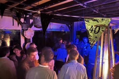 Entrée d'un café avec une terrasse équipée d'un parasol orange et des fauteuils en osier, sous un ciel ensoleillé.