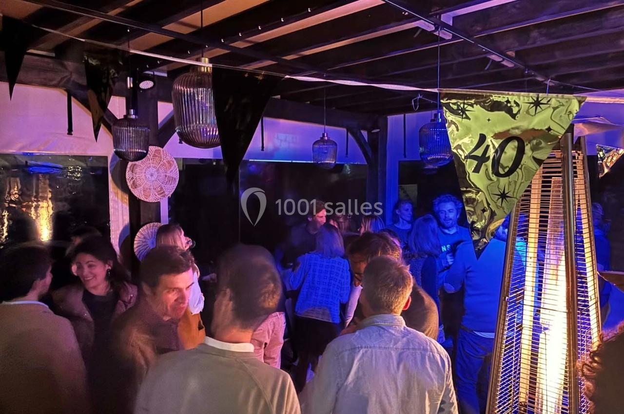 Groupe de personnes discutant et dansant lors d'une fête en soirée, sous une lumière tamisée et des décorations.