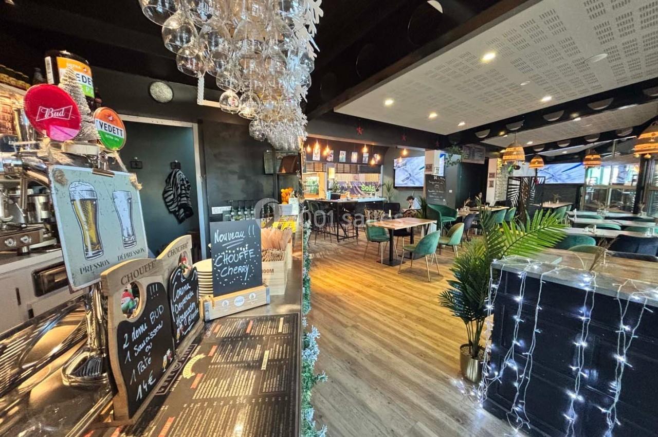 Intérieur d'un bar-restaurant avec comptoir, tables, chaises, décorations lumineuses et ambiance chaleureuse.