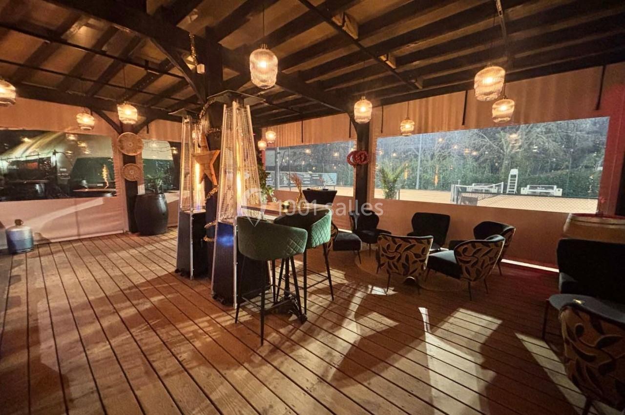 Terrasse couverte en bois avec éclairage chaleureux, chaises design et vue sur un extérieur sombre.