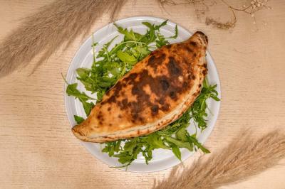 Entrée d'un café avec une terrasse équipée d'un parasol orange et des fauteuils en osier, sous un ciel ensoleillé.