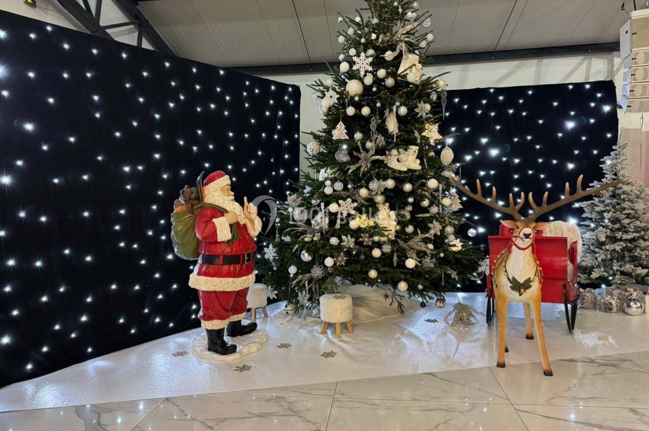 Décor de Noël avec un sapin illuminé, un Père Noël, un renne en bois et un fond étoilé dans un espace intérieur.