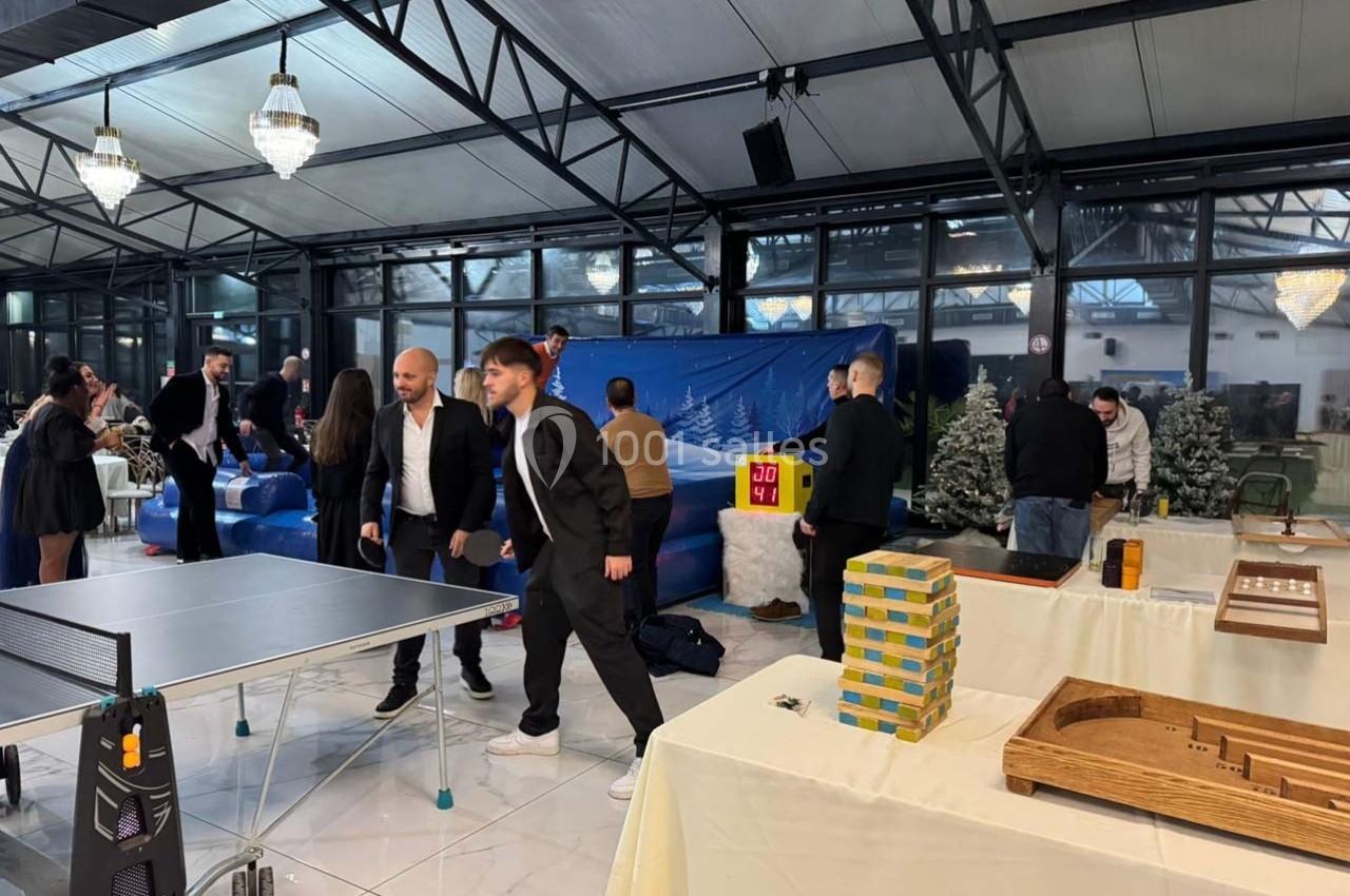 Des personnes jouent et discutent autour de jeux de société et d'une table de ping-pong dans une salle lumineuse.