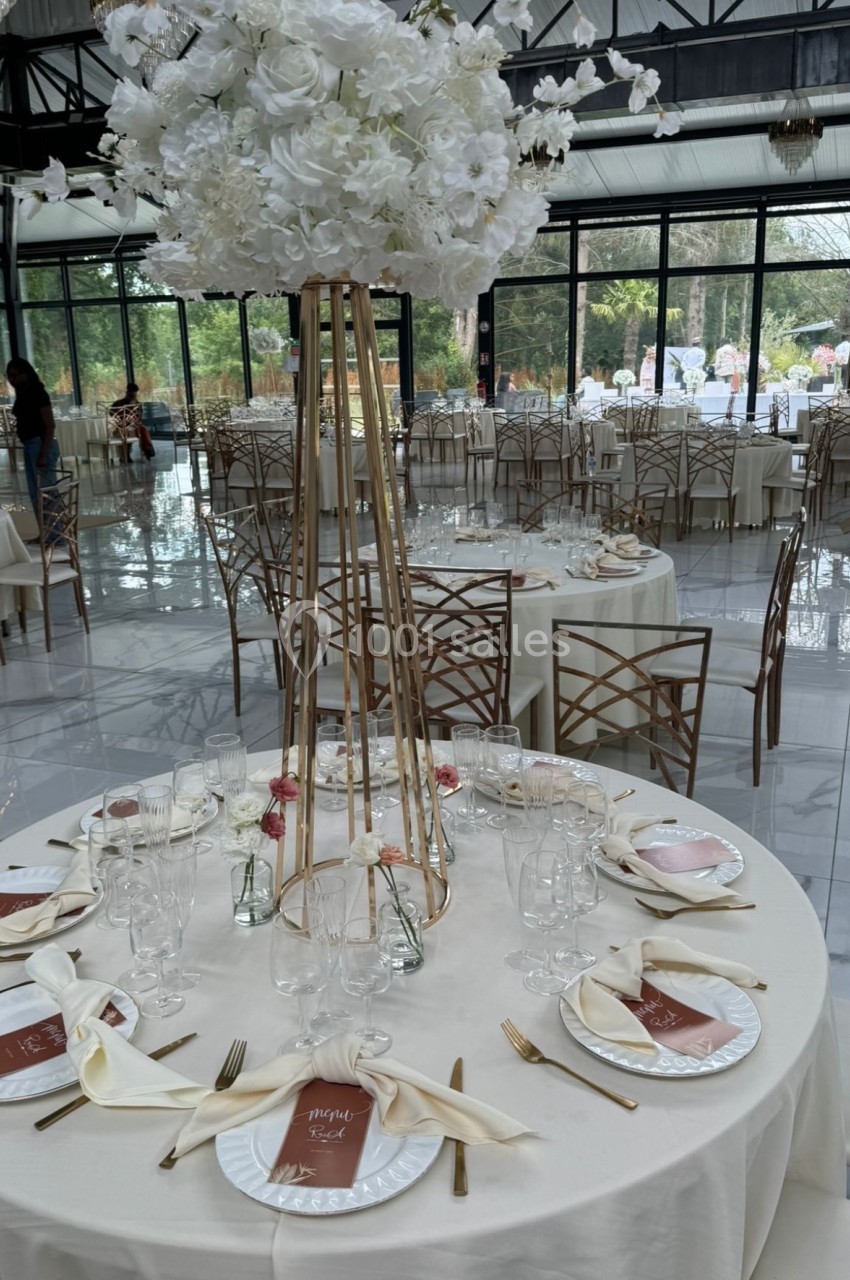Table de réception élégante avec nappes blanches, vaisselle raffinée et centre de table floral sur pied doré.
