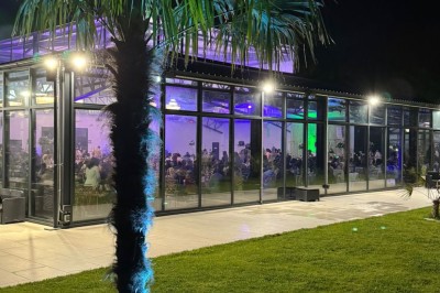 Voiture ancienne blanche stationnée devant une véranda moderne, entourée de végétation et d'arbres.