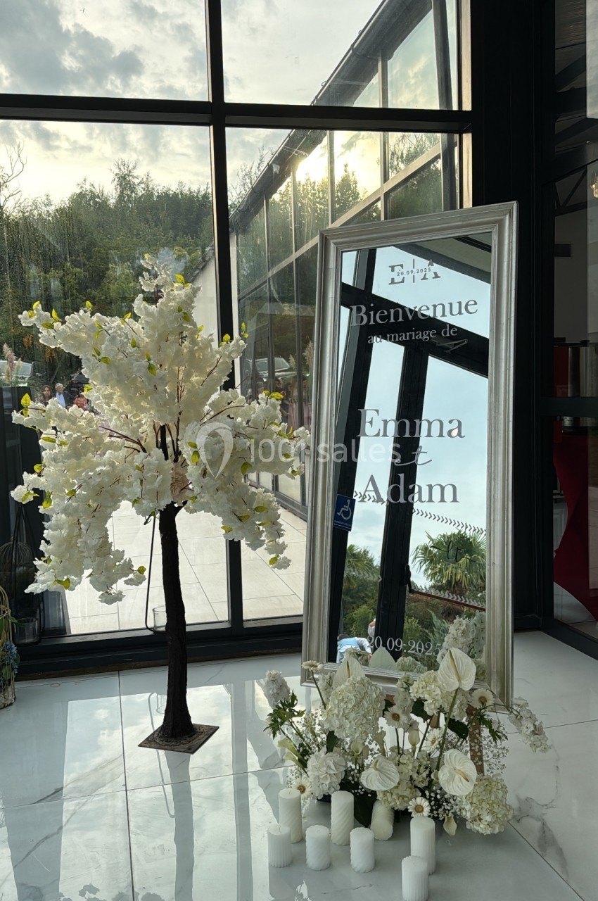 Arbre décoratif et miroir avec message de bienvenue pour un mariage, entourés de fleurs blanches et bougies.