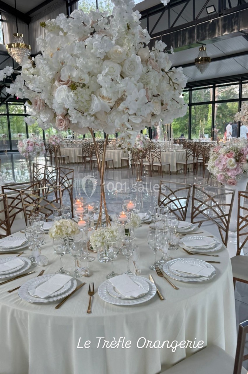 Centre de table floral blanc et rose sur une table dressée dans une salle lumineuse avec grandes baies vitrées.