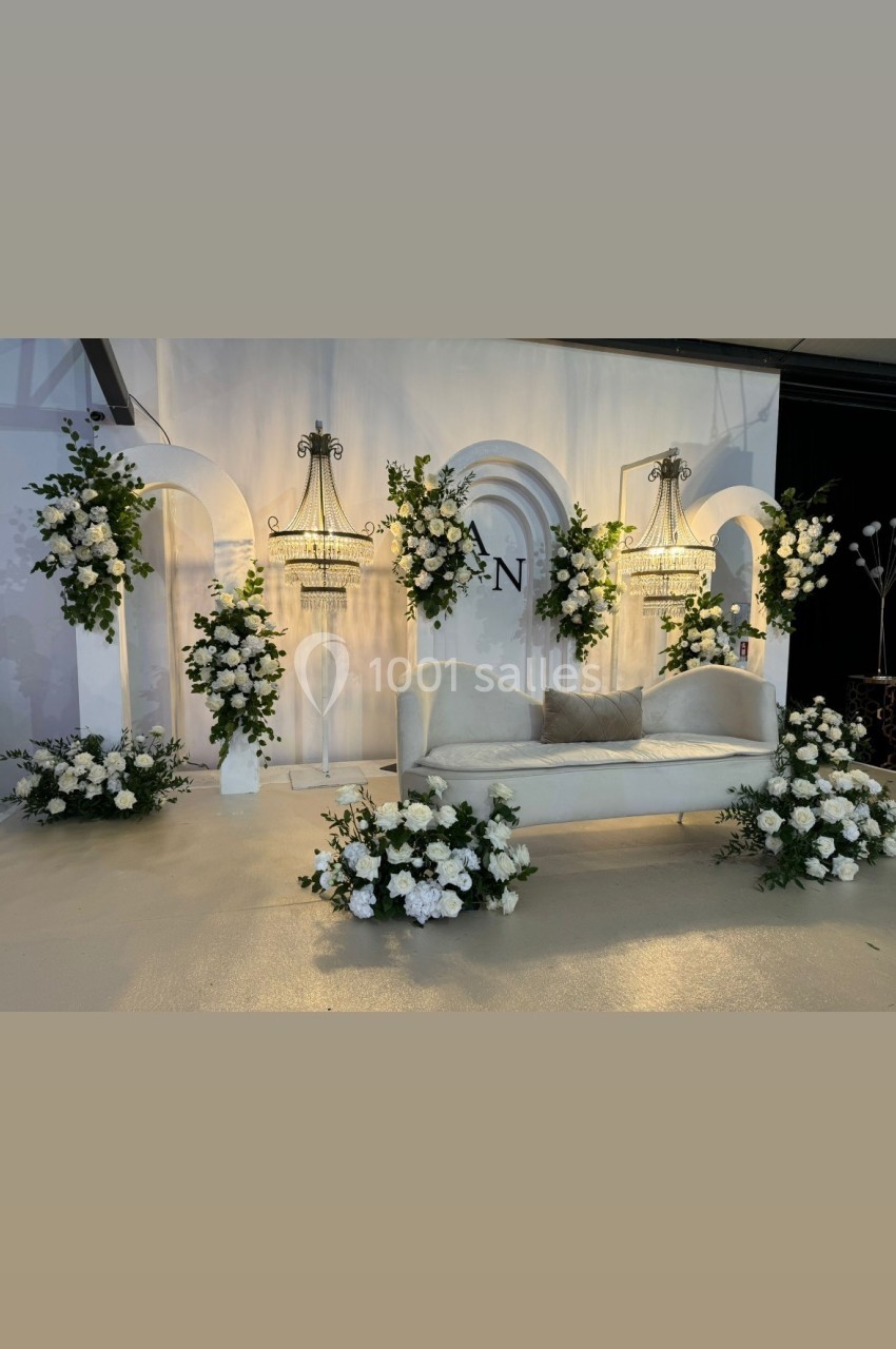Décor élégant avec un canapé blanc entouré de compositions florales blanches et de lustres suspendus.