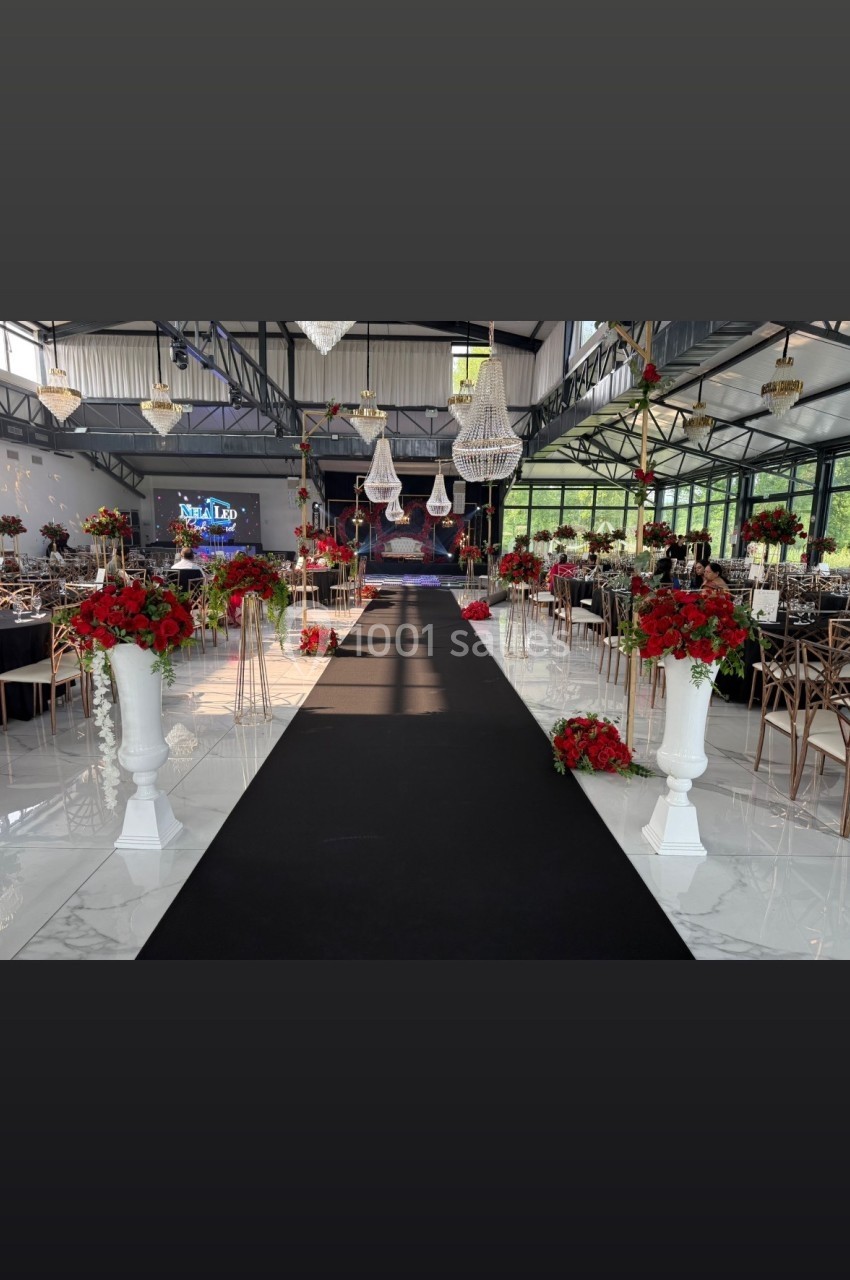 Allée centrale décorée de fleurs rouges et blanches dans une salle de réception lumineuse avec lustres suspendus.