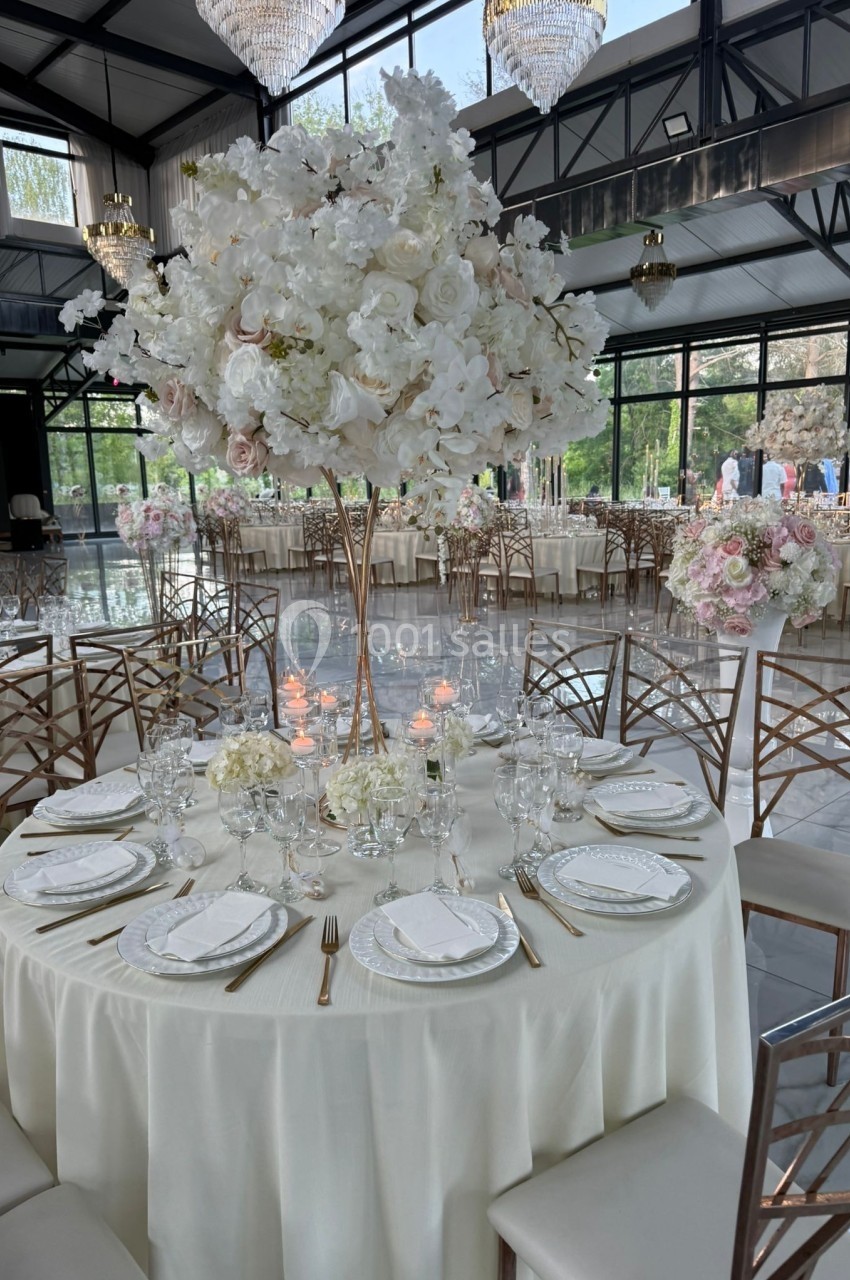 Table élégamment dressée avec nappes blanches, vaisselle raffinée et centre de table floral imposant dans une salle de…