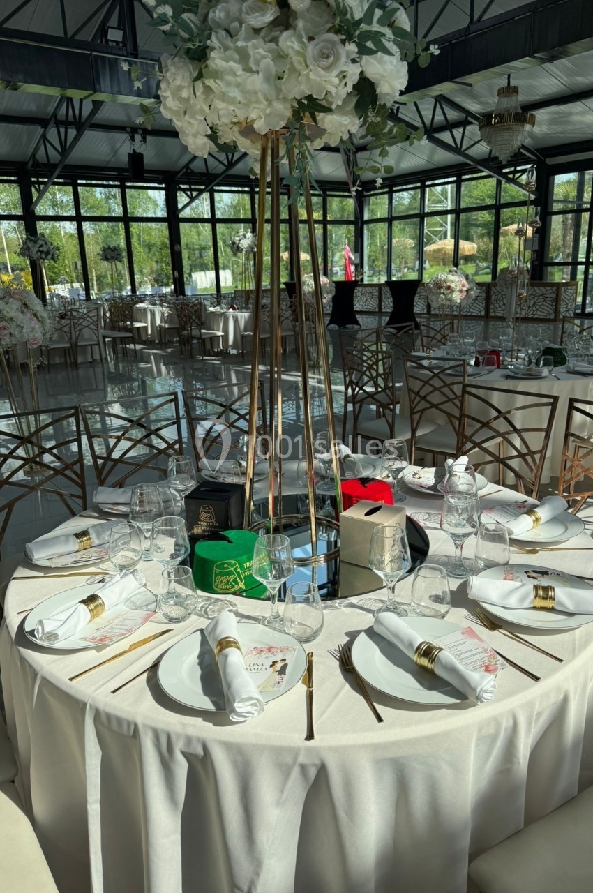 Table ronde élégamment dressée avec nappes blanches, vaisselle raffinée et centre de table floral dans une salle lumineuse.