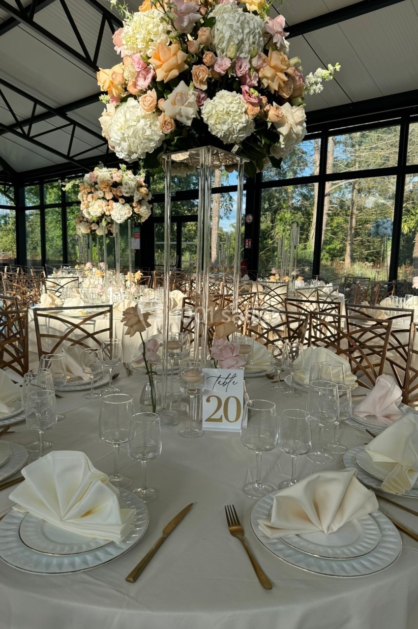Table décorée pour un événement avec nappes blanches, serviettes pliées, vaisselle élégante et centre de table floral.