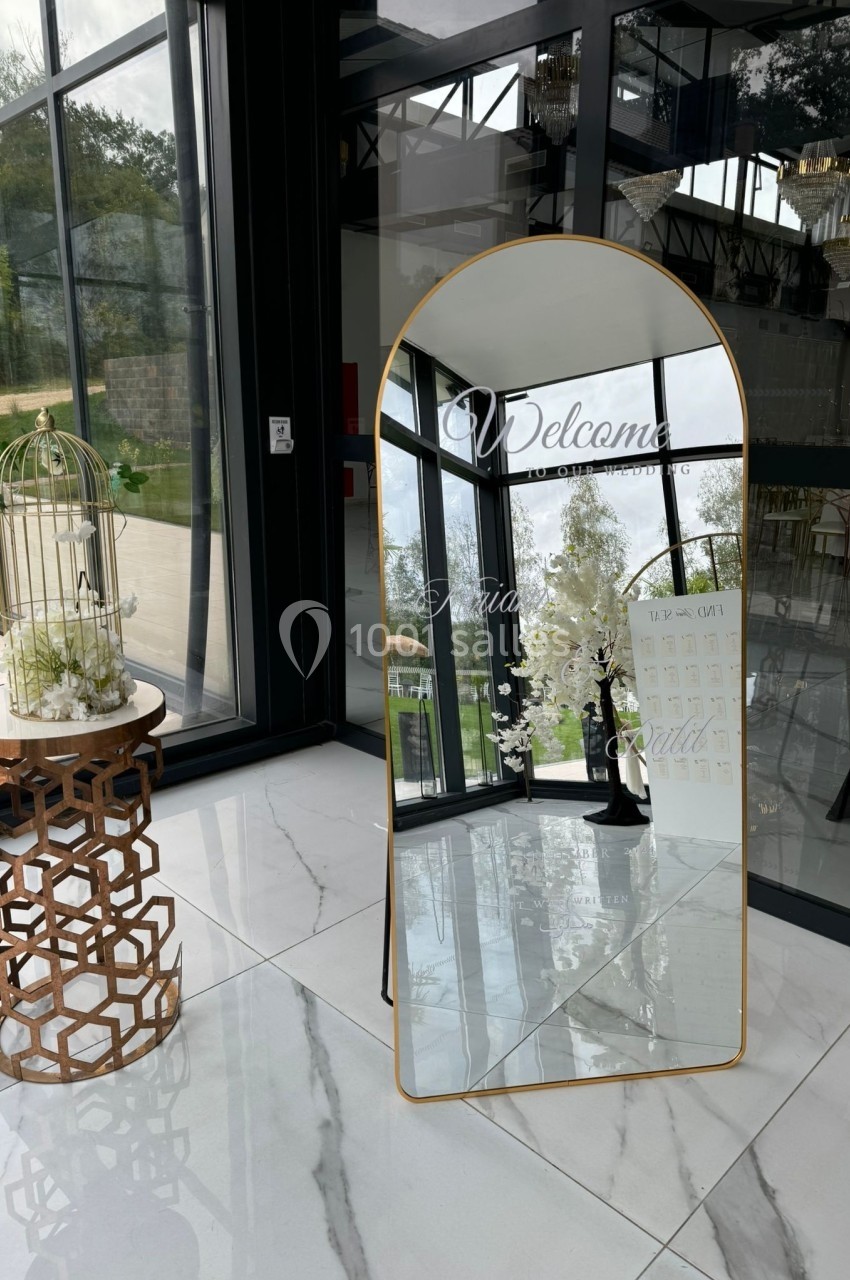 Miroir doré sur pied avec inscription de bienvenue, placé près d'une table décorative et d'une cage à oiseaux, dans un…