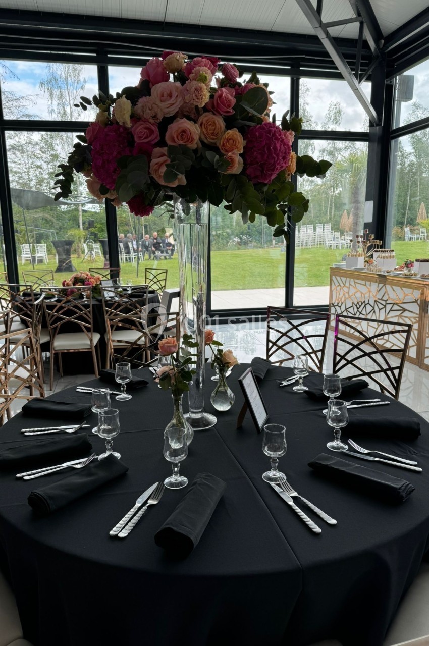 Table ronde dressée avec une nappe noire, couverts disposés, et un grand bouquet de fleurs colorées au centre.