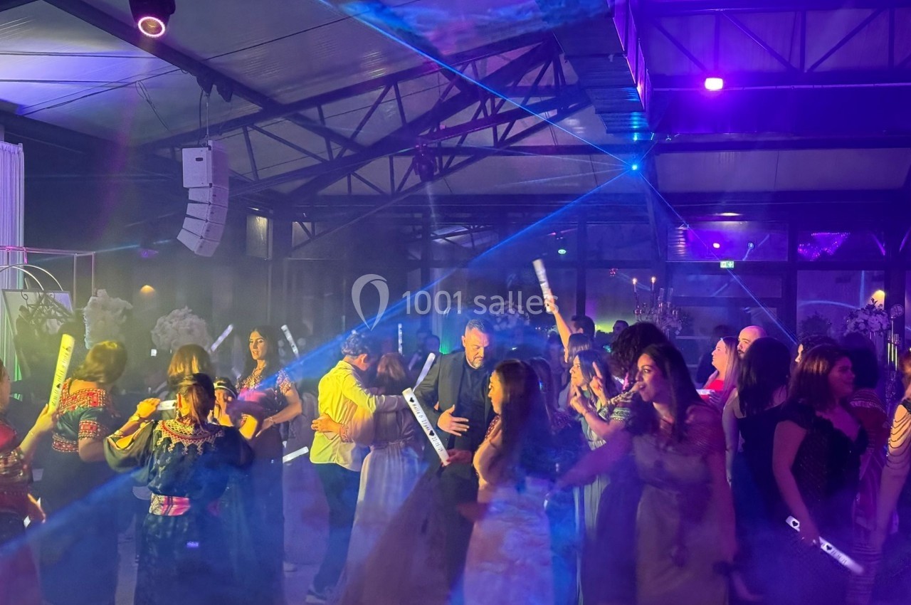 Des personnes dansent sous des lumières colorées et des faisceaux laser dans une salle de fête.