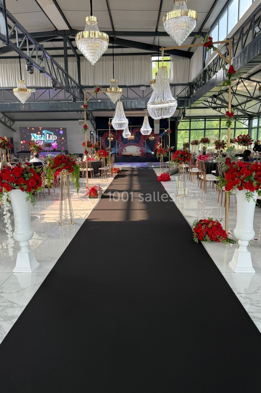 Allée centrale décorée de fleurs rouges et blanches dans une salle de réception avec lustres suspendus.
