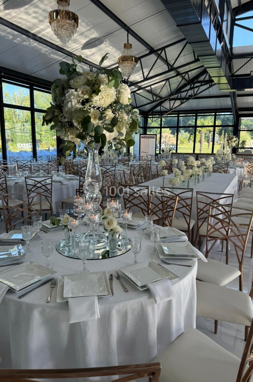 Salle de réception lumineuse avec tables décorées de fleurs blanches, chandeliers et vaisselle élégante.