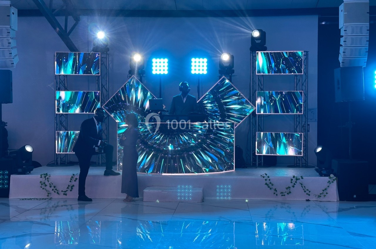 Un DJ mixe sur une scène illuminée avec des écrans LED colorés, devant un couple dansant sur une piste brillante.