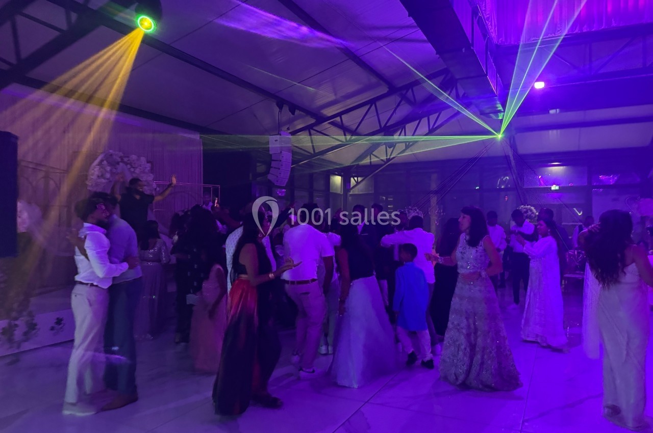 Des personnes dansent sous des jeux de lumières colorées dans une salle de réception spacieuse.