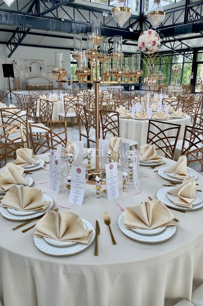 Table élégamment dressée avec nappes blanches, serviettes pliées, vaisselle raffinée et décorations florales dans une salle…