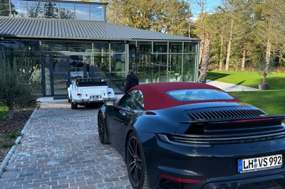 Voiture ancienne blanche stationnée devant une véranda moderne, entourée de végétation et d'arbres.