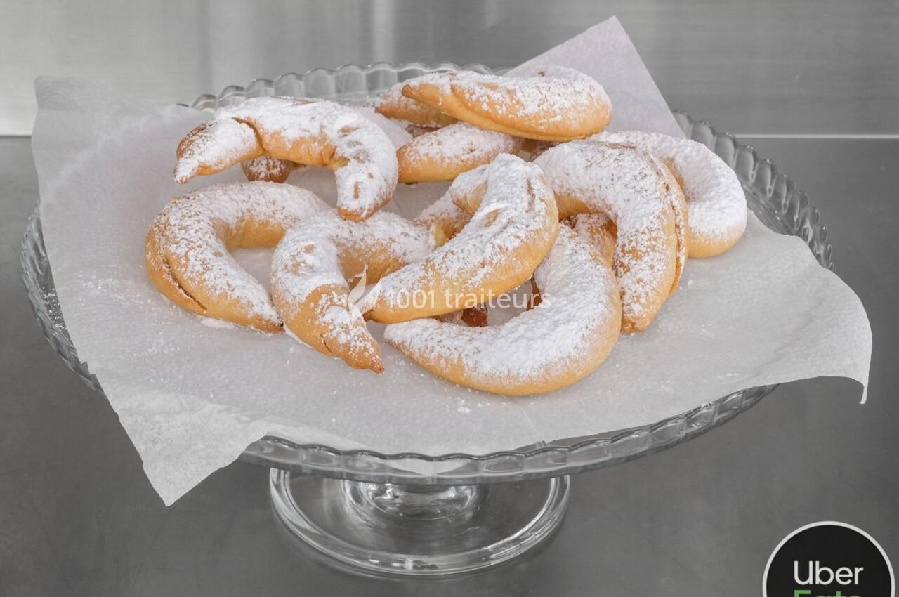 Assortiment de croissants en pâte sucrée saupoudrés de sucre glace, présentés sur un plat en verre.