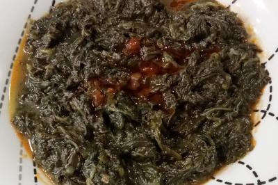 Plat de feuilles de légumes mijotées dans une sauce épicée, présenté dans une assiette blanche.