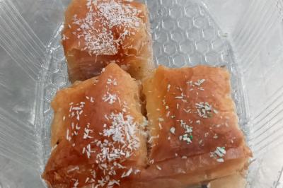 Trois parts de pâtisserie feuilletée dorée, saupoudrées de noix de coco râpée, dans un contenant transparent.