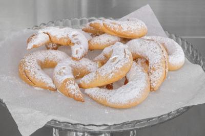 Assortiment de croissants sablés saupoudrés de sucre glace, disposés sur un plat en verre avec du papier cuisson.
