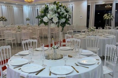 Centre de table avec des roses blanches et feuillage sur un support en verre, dans une salle de réception élégante.