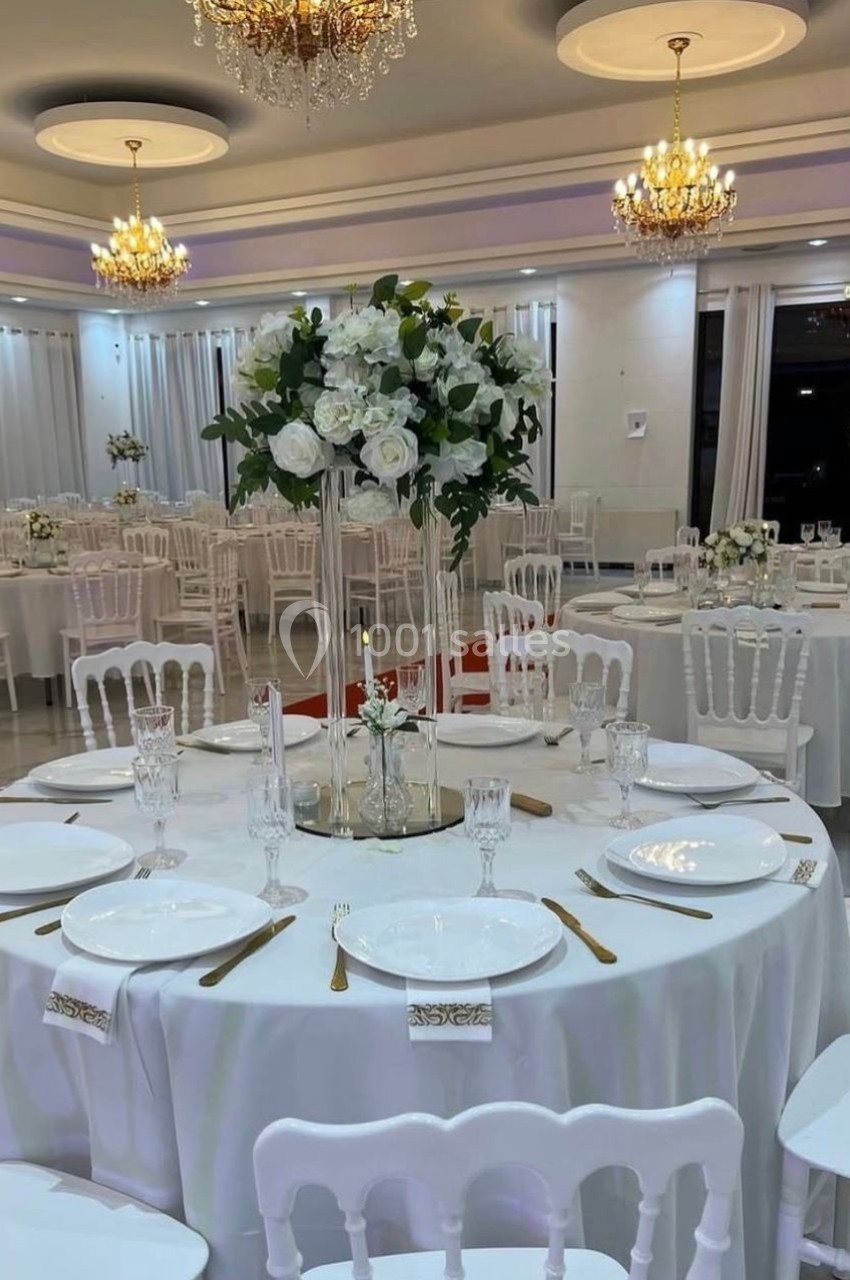 Salle de réception élégante avec tables rondes dressées, nappes blanches, chandeliers et décorations florales.