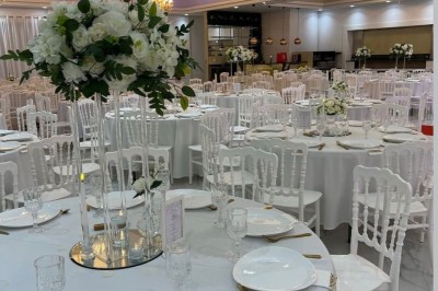 Centre de table avec des roses blanches et feuillage sur un support en verre, dans une salle de réception élégante.