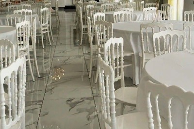 Salle de réception élégante avec tables rondes décorées de fleurs blanches et chaises blanches, éclairée par des lustres.