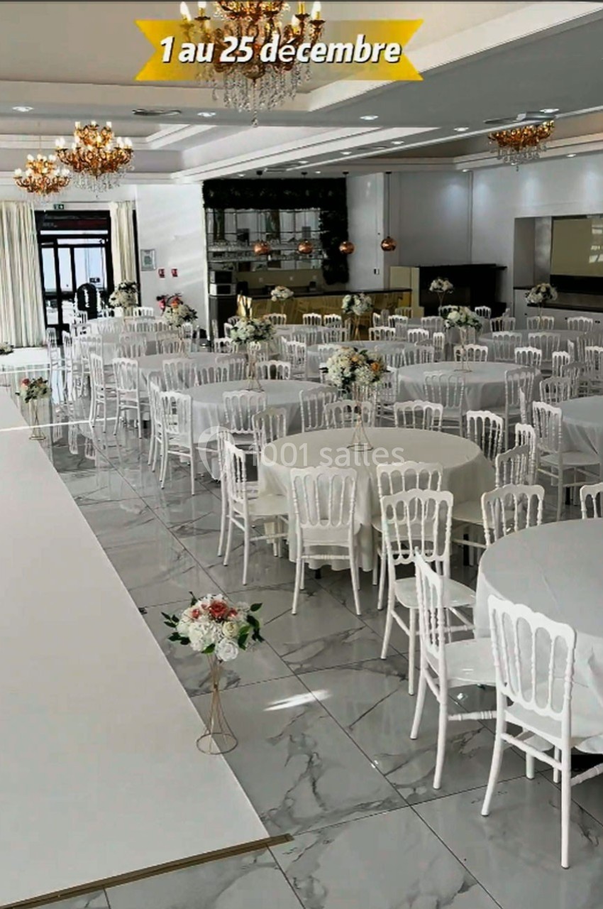 Salle de réception élégante avec tables rondes décorées de fleurs blanches et chaises blanches, éclairée par des lustres.