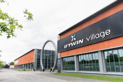 Salle vide avec sol en béton, grandes baies vitrées, murs blancs et plafond industriel avec éclairage suspendu.