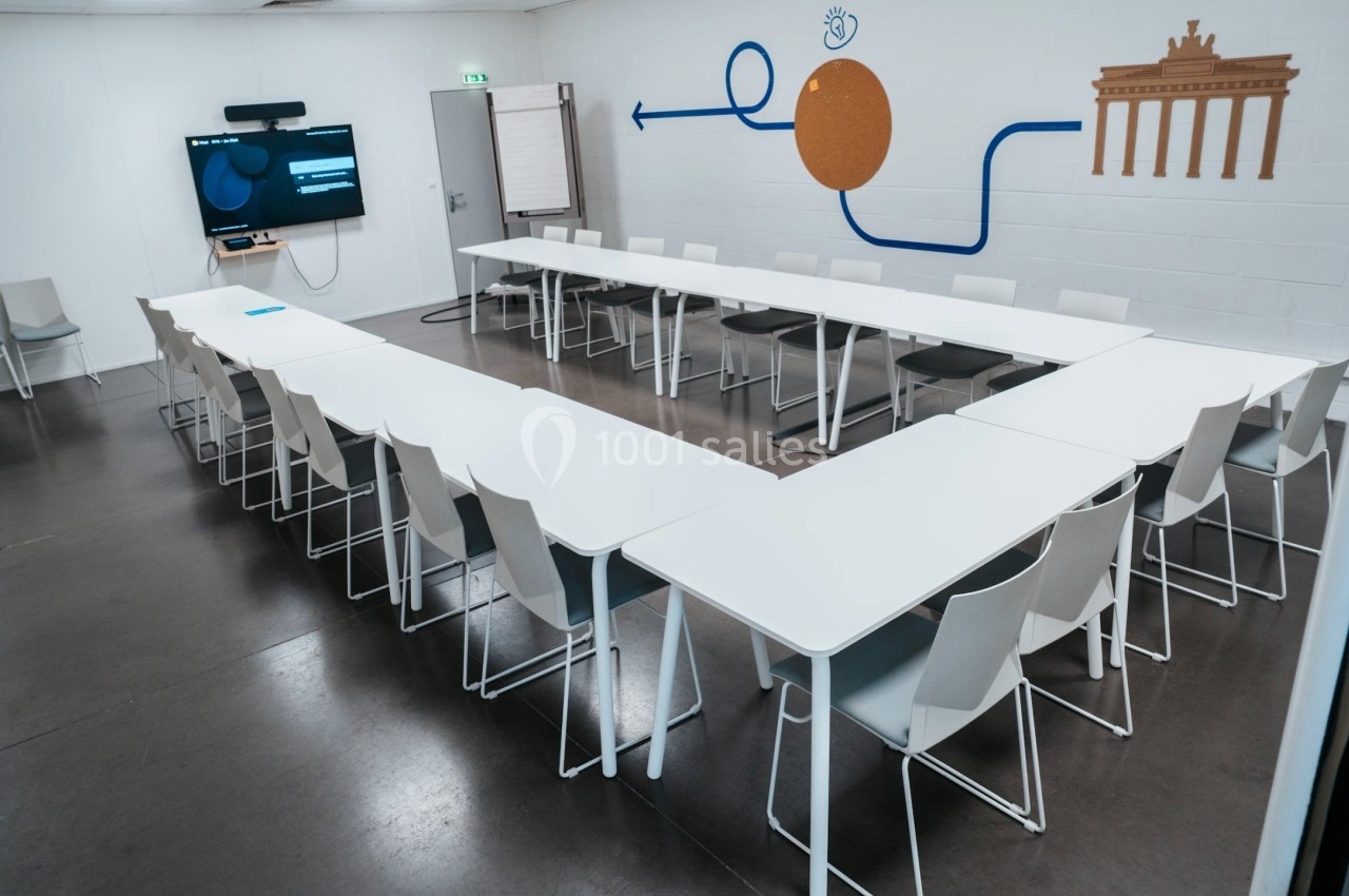 Salle de réunion avec tables disposées en U, chaises blanches, écran mural et décorations sur le mur.