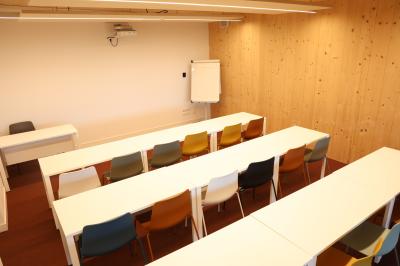 Salle de réunion lumineuse avec tables blanches, chaises orange et un tableau blanc sur pied.