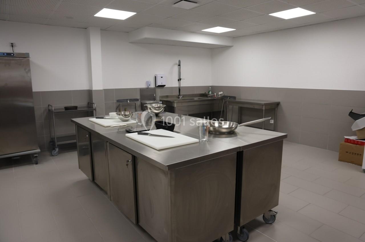 Cuisine professionnelle avec plan de travail en inox, évier, ustensiles et équipements de préparation.