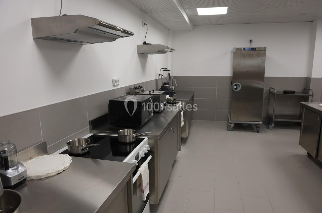 Cuisine professionnelle équipée avec plans de travail en inox, plaques de cuisson, hotte, réfrigérateur et divers appareils.